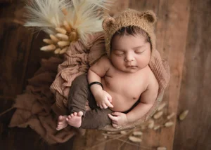 Newborn in a brown bear-ear knit hat on a brown wrap with dried grasses on dark wood, Bay Area newborn photography session