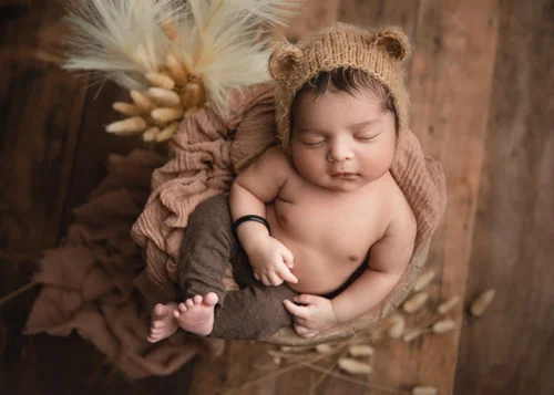 Newborn in a brown bear-ear knit hat on a brown wrap with dried grasses on dark wood, Bay Area newborn photography session
