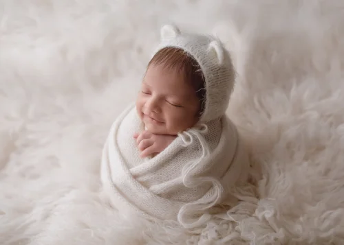 Smiling newborn in a white bear-ear bonnet swaddled on a white fluffy rug, Bay Area newborn photographer studio session