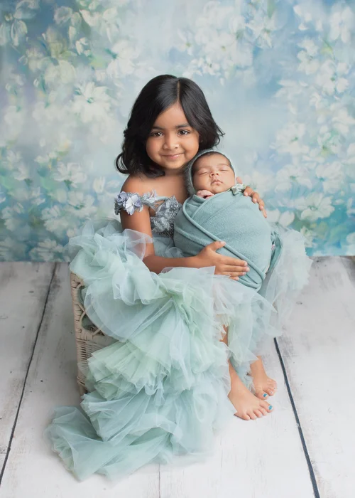 Big sister in a teal tulle dress holding her newborn sibling in a teal wrap, Mountain View newborn photographer