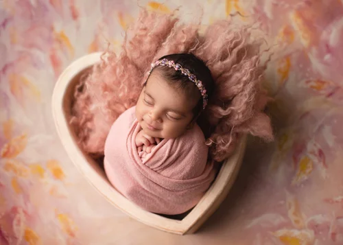 Newborn girl swaddled in pink in a cream heart-shaped bowl on a warm painted backdrop, Mountain View newborn photographer