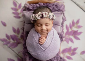 Smiling newborn girl in a lavender wrap with a flower crown on a purple leaf bed, Mountain View newborn photographer