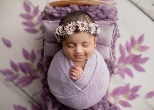 Smiling newborn girl in a lavender wrap with a flower crown on a purple leaf bed, Mountain View newborn photographer