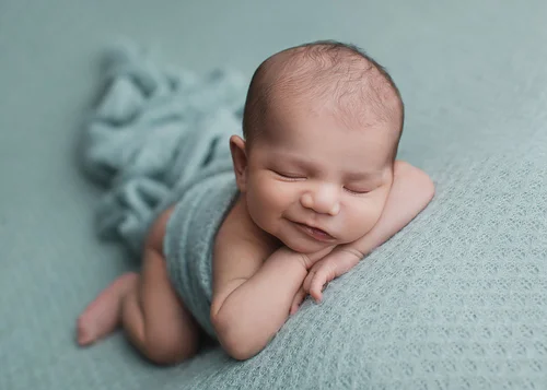 Newborn in a teal wrap resting his chin on his hands on a sea-green blanket, Bay Area newborn photography session