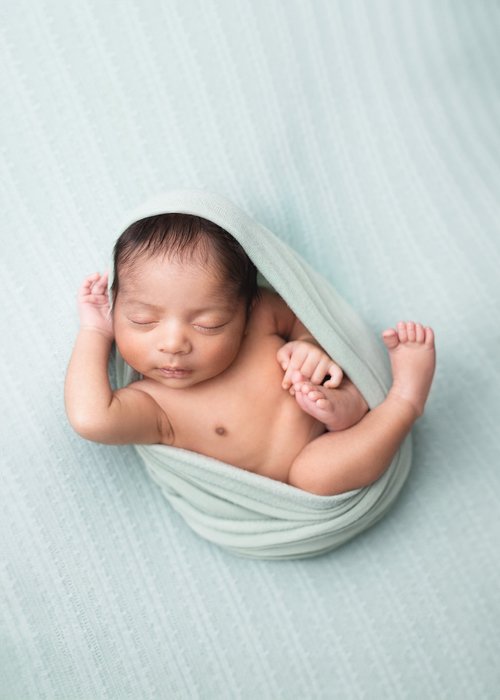 Newborn swaddled in pale green with arms raised on a mint backdrop, Bay Area newborn photographer studio session