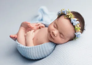 Newborn girl with a blue flower crown in a blue knit wrap on a pale blue backdrop, Mountain View newborn photographer