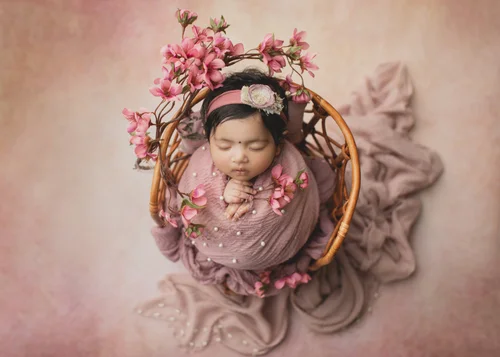 Overhead view of a newborn wrapped in pink in a rattan bowl with pink blossoms, Bay Area newborn photography session