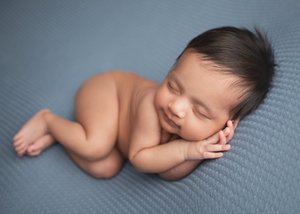 Newborn sleeping bare with hands tucked under his cheek on a blue textured blanket, Bay Area newborn photographer studio session