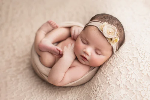 Newborn girl with a cream flower headband curled in a cream wrap on soft lace, Bay Area newborn photographer studio session
