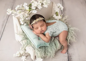 Newborn girl with a flower headband sleeping on a white bed prop with white blossoms, Mountain View newborn photographer