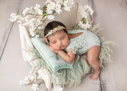Newborn girl with a flower headband sleeping on a white bed prop with white blossoms, Mountain View newborn photographer