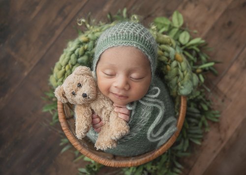 Newborn in a mint knit bonnet hugging a teddy bear in a basket with greenery, Mountain View newborn photographer