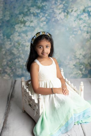 Big sister in a white dress and flower headband sitting on a white vintage bed prop, Mountain View newborn photography studio