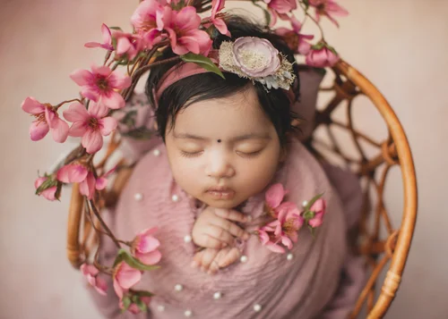 Newborn girl swaddled in pink with blossoms in a rattan bowl on a blush backdrop, Mountain View newborn photography studio