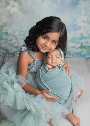 Big sister in a teal tulle dress cuddling her newborn sibling in a teal wrap, Bay Area newborn photographer studio session