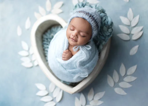 Newborn in a light blue knit bonnet swaddled in a white heart bowl on a blue backdrop, Bay Area newborn photography session