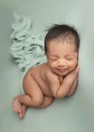 Smiling newborn lying on a mint green blanket with hands under his chin, Bay Area newborn photography session