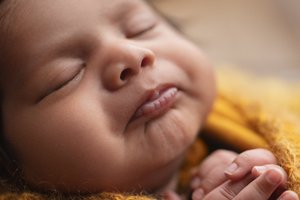Close-up of a sleeping newborn with a soft smile on a mustard yellow blanket, Mountain View newborn photography studio