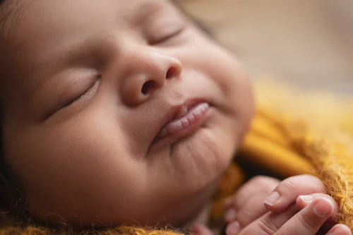 Close-up of a sleeping newborn with a soft smile on a mustard yellow blanket, Mountain View newborn photography studio