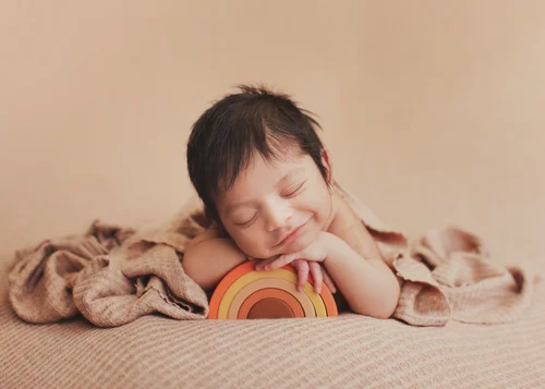 Newborn resting his head on his hands next to a small rainbow stacker toy, Bay Area newborn photographer studio session