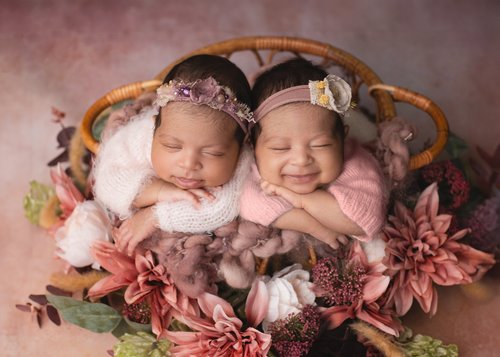 Twin newborn girls with flower headbands sleeping side by side in a basket of dusty pink flowers, Mountain View newborn photography studio