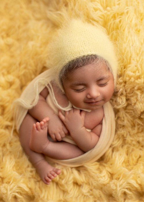 Newborn in a cream knit bonnet curled on a yellow fluffy rug, Bay Area newborn photographer studio session