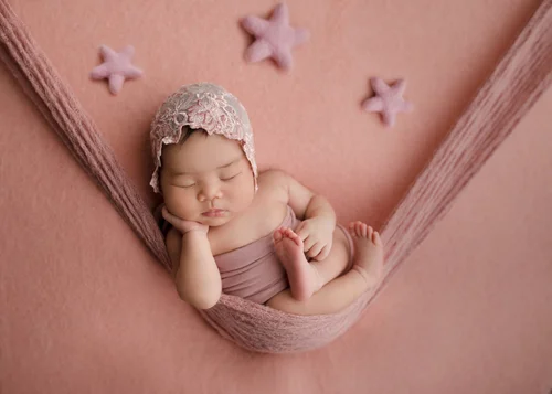 Newborn in a lace bonnet resting her cheek on her hand in a pink hammock wrap with stars, Mountain View newborn photographer