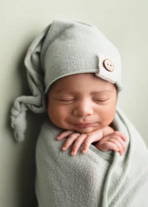 Newborn in a sage green sleepy cap with a wooden button, hands folded, swaddled in sage, Mountain View newborn photography studio
