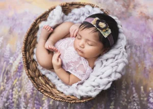 Newborn girl with a floral headband in a woven basket on a lavender flower backdrop, Mountain View newborn photographer