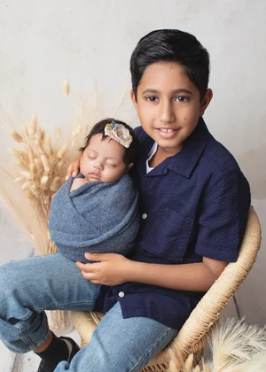 Smiling big brother in a navy shirt holding his newborn sibling wrapped in blue, Mountain View newborn photographer