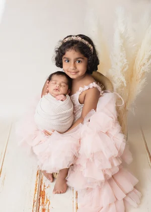 Big sister in a pink ruffled dress hugging her newborn sibling wrapped in cream, Mountain View newborn photographer