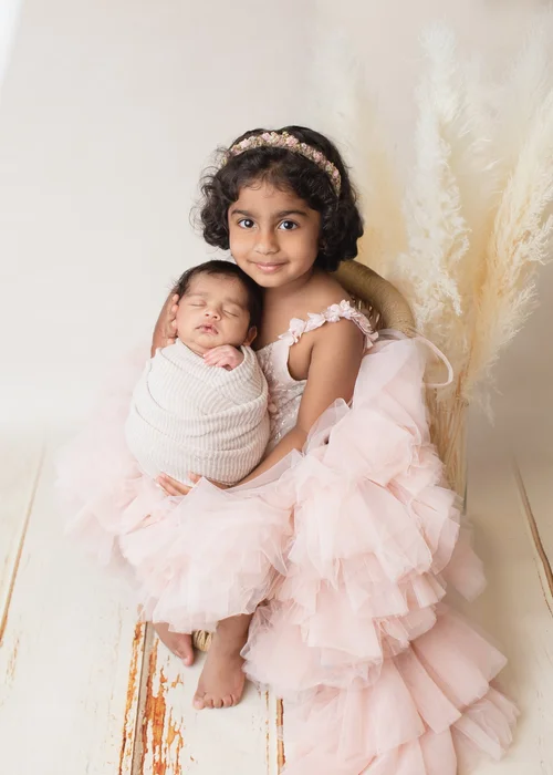 Big sister in a pink ruffled dress hugging her newborn sibling wrapped in cream, Mountain View newborn photographer