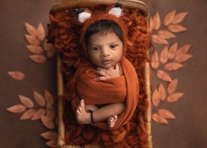 Newborn in a fox-ear hat swaddled in rust orange in a wooden crate with orange leaves, Bay Area newborn photography session