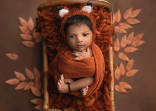 Newborn in a fox-ear hat swaddled in rust orange in a wooden crate with orange leaves, Bay Area newborn photography session