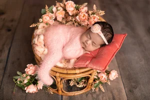 Newborn girl in pink fluffy knit and a flower crown on a rattan chair with pink roses, Mountain View newborn photography studio