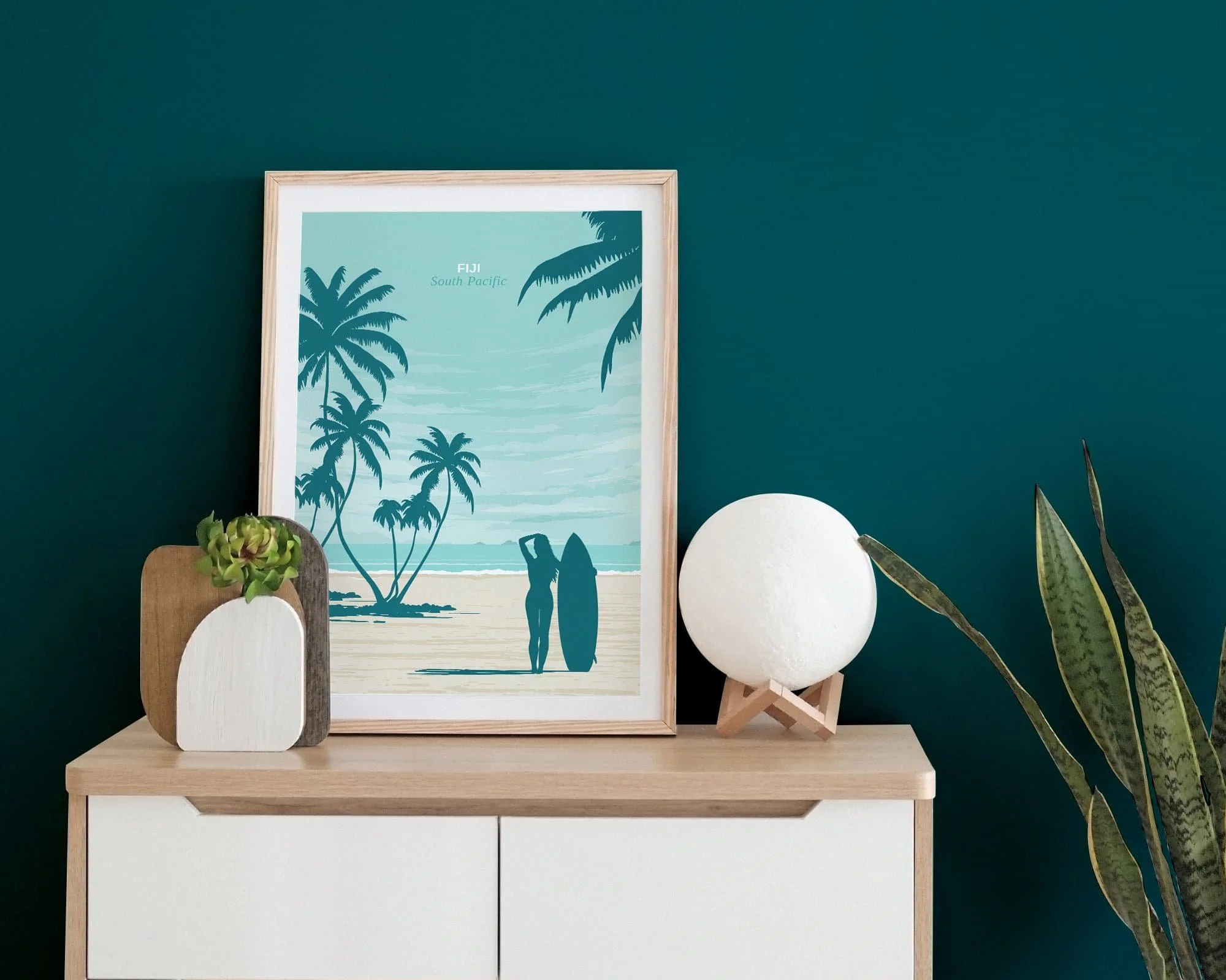 Framed illustration art prints of Fiji on a sideboard with a teal wall behind.