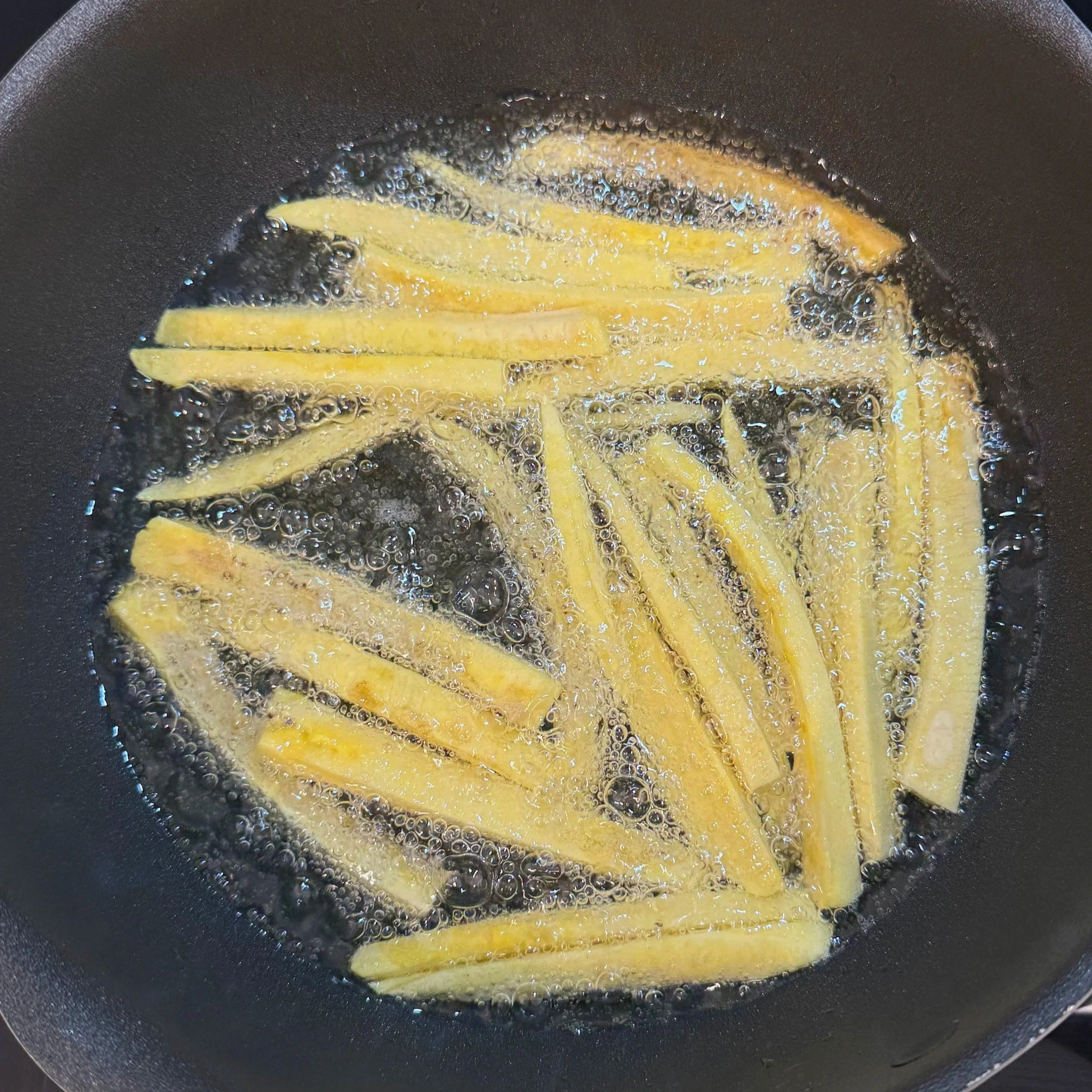 Plantain frites frying in a pan of hot oil