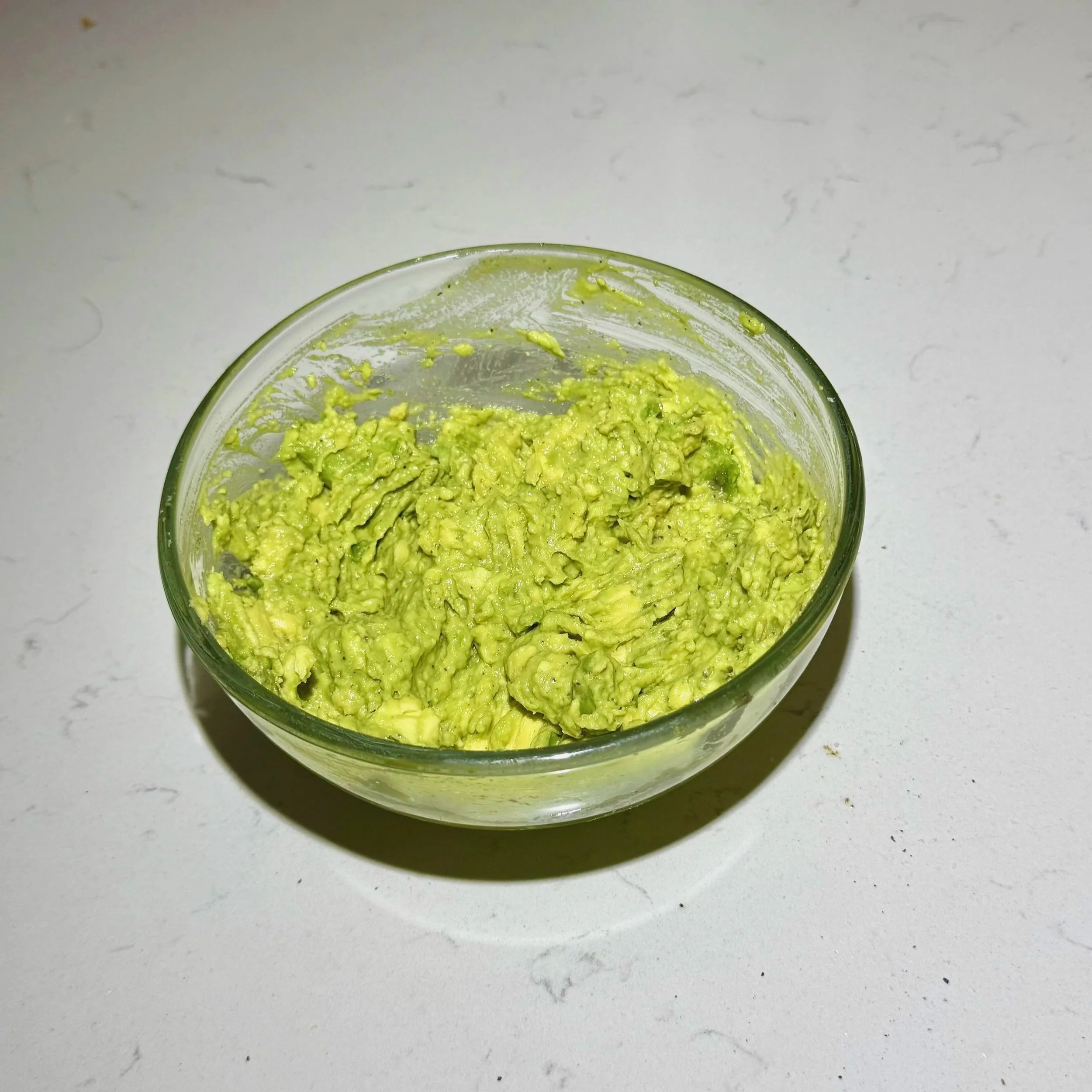 Creamy mashed avocado seasoned with salt and pepper in a white bowl for tuna rice stack layers