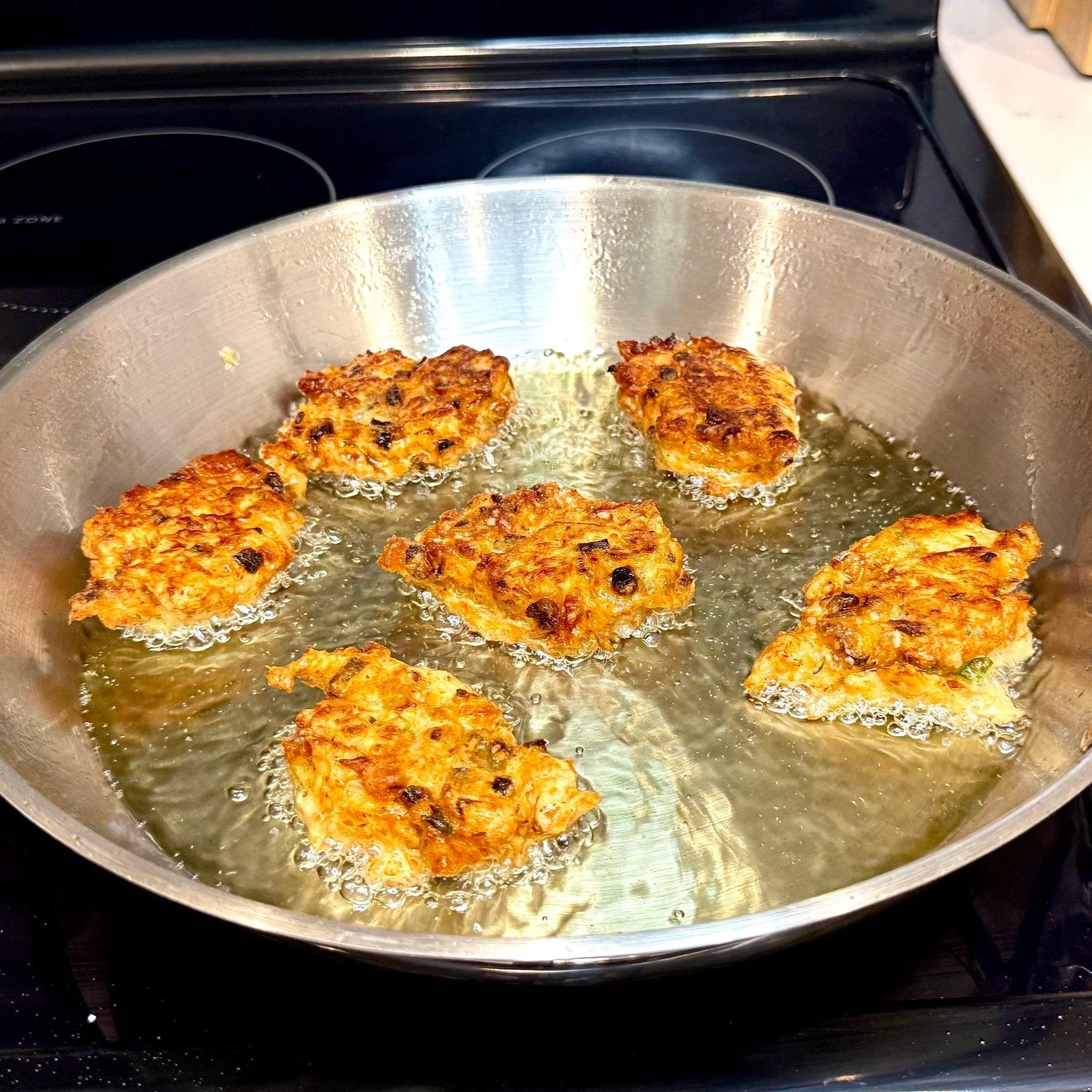Saltfish fritters flipped in oil frying until evenly golden and crispy.