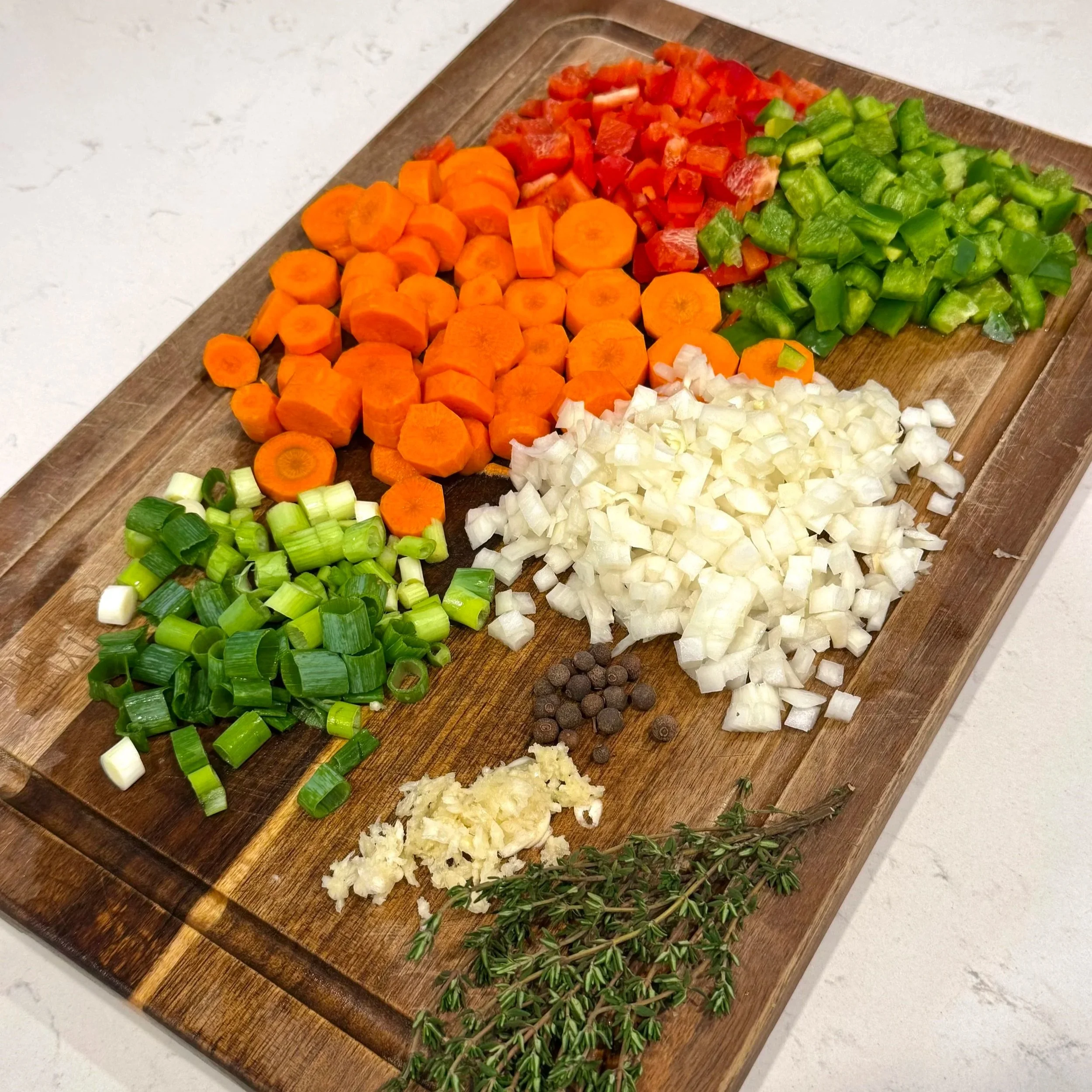 Chopped vegetables including carrots, bell peppers, onions, scallions, garlic, and thyme on a wooden board for Jamaican oxtail