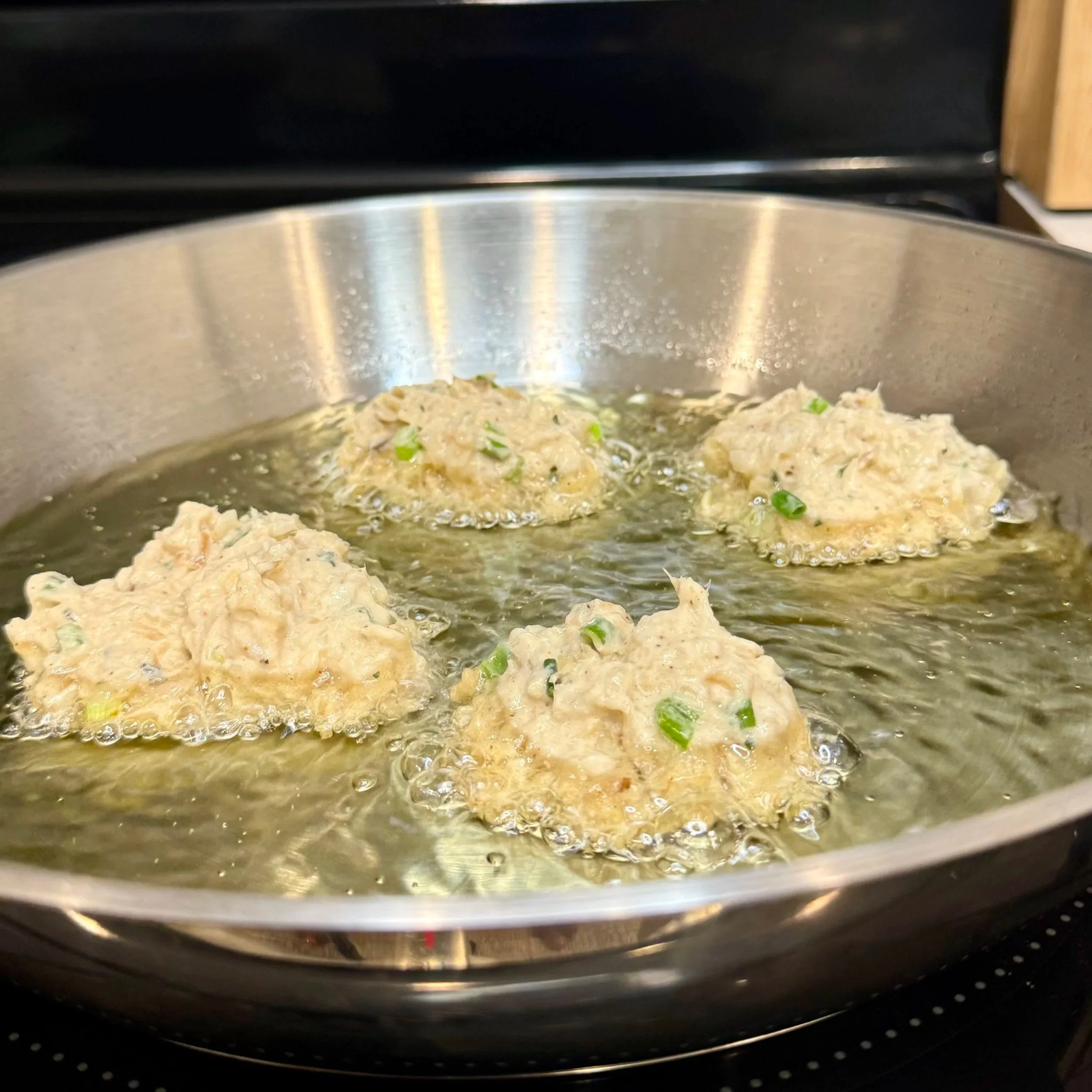 Saltfish fritter batter sizzling in hot oil in a skillet.