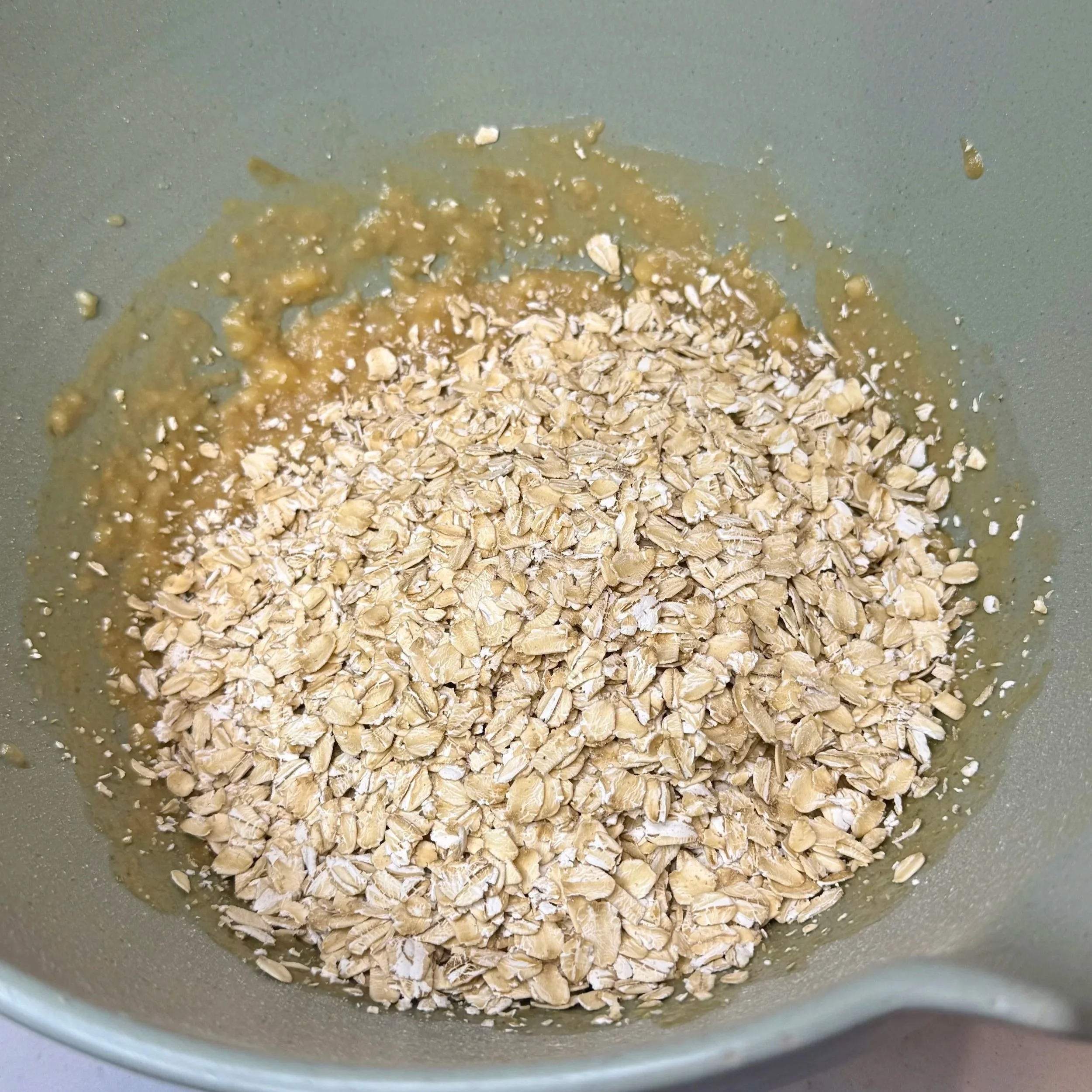 Rolled oats, mashed bananas, nut butter, chocolate chips, and dried fruit in a mixing bowl