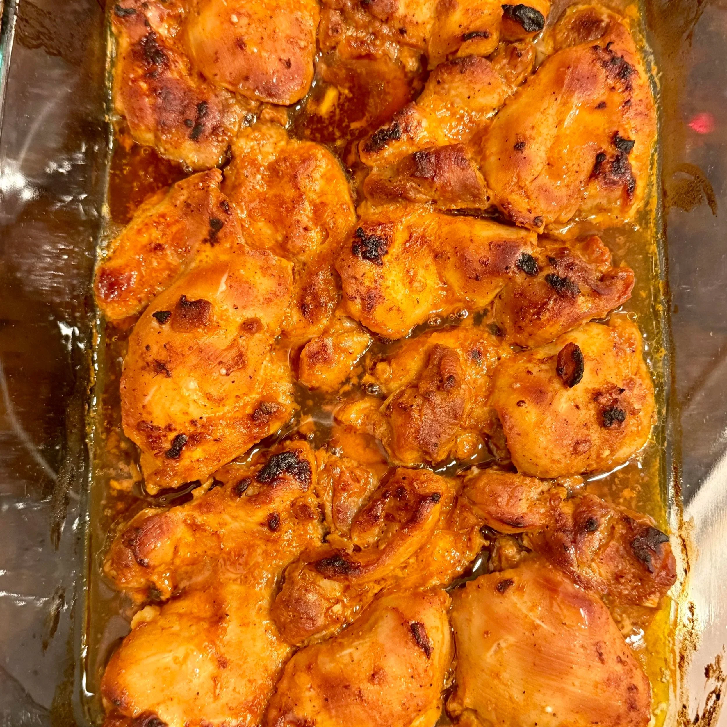 Chicken thighs baking in the oven, caramelizing with a glossy red glaze.