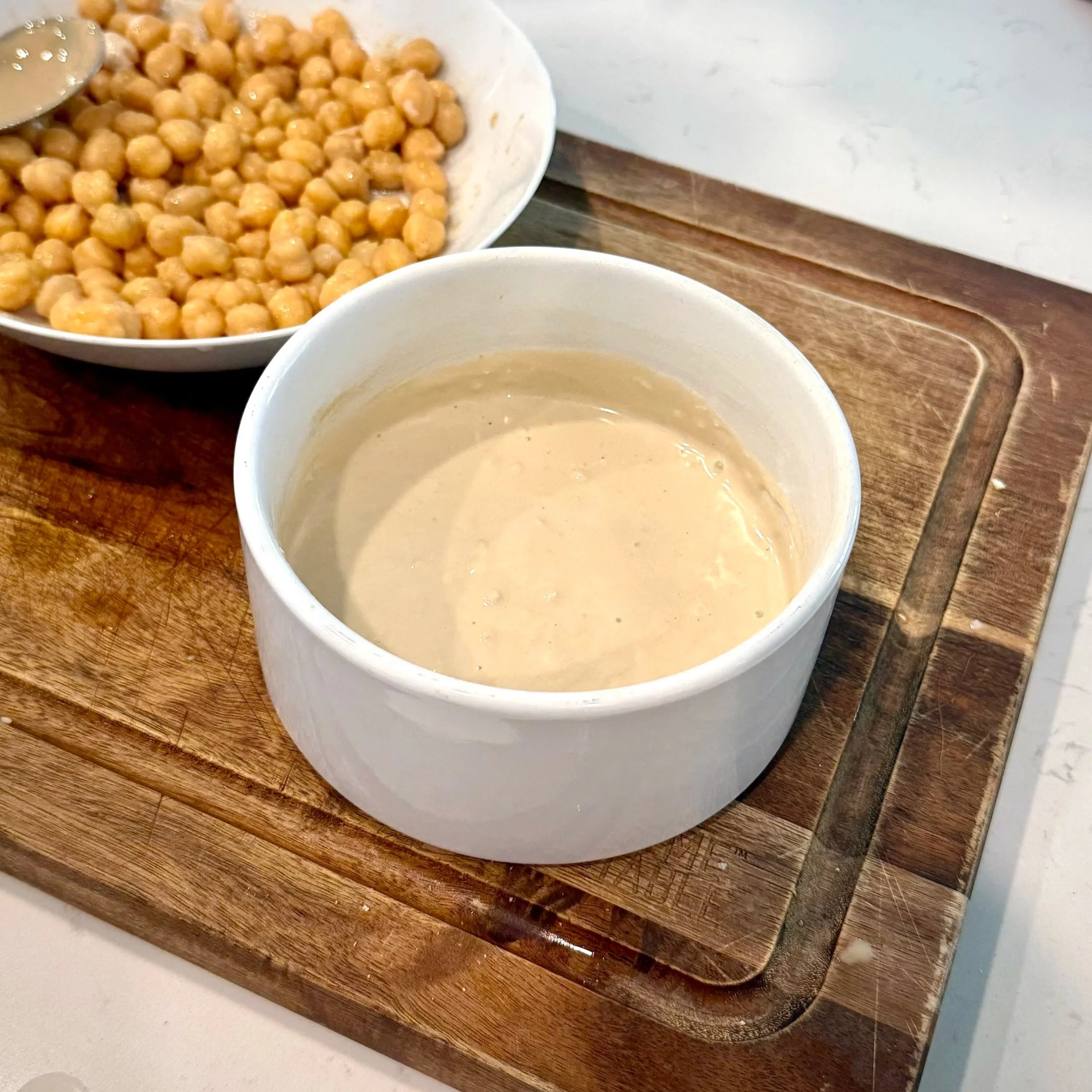 Bowl of creamy tahini dressing mixed with ginger, garlic, rice vinegar, and sriracha.