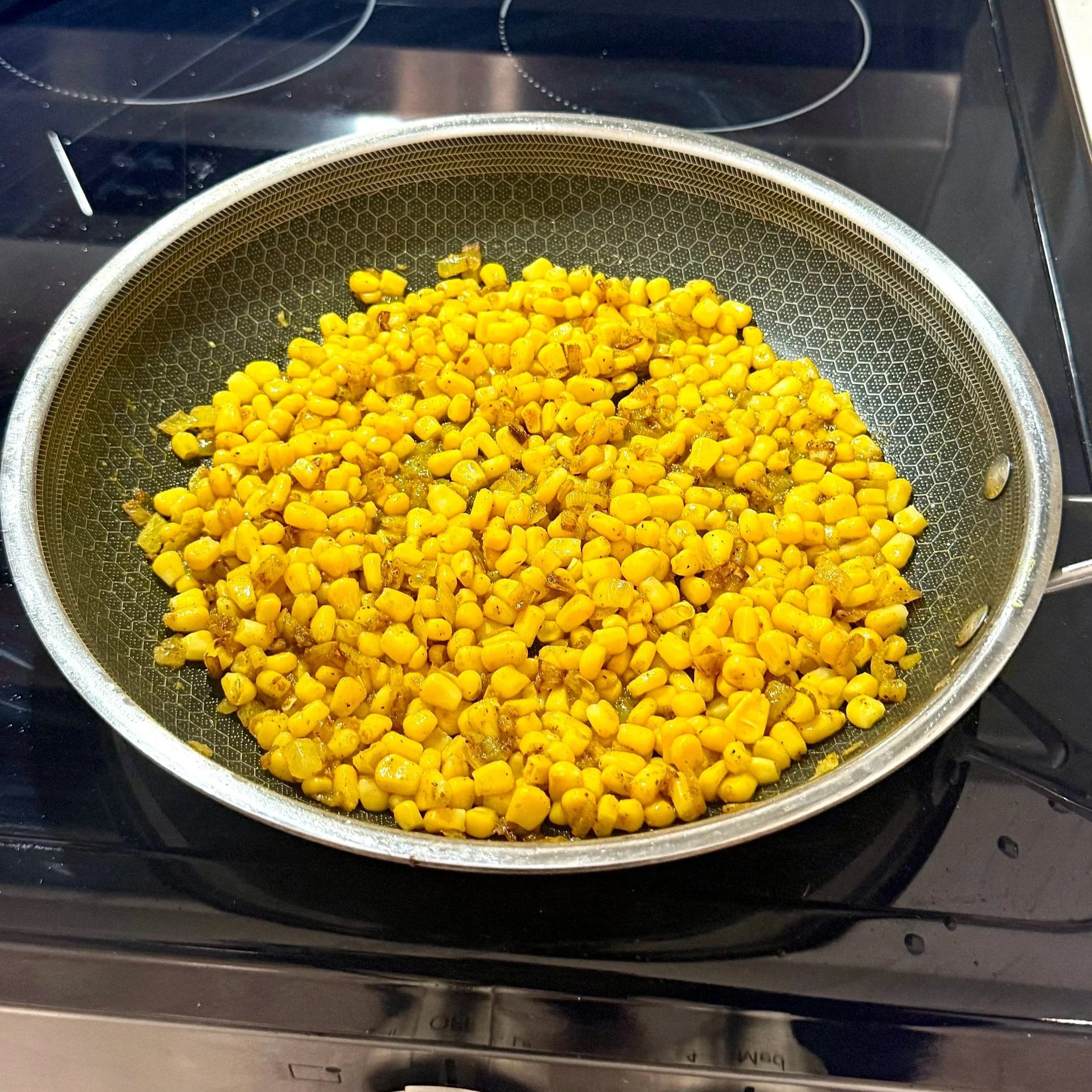 Corn relish cooking in a skillet with onions, ginger, and warm spices.