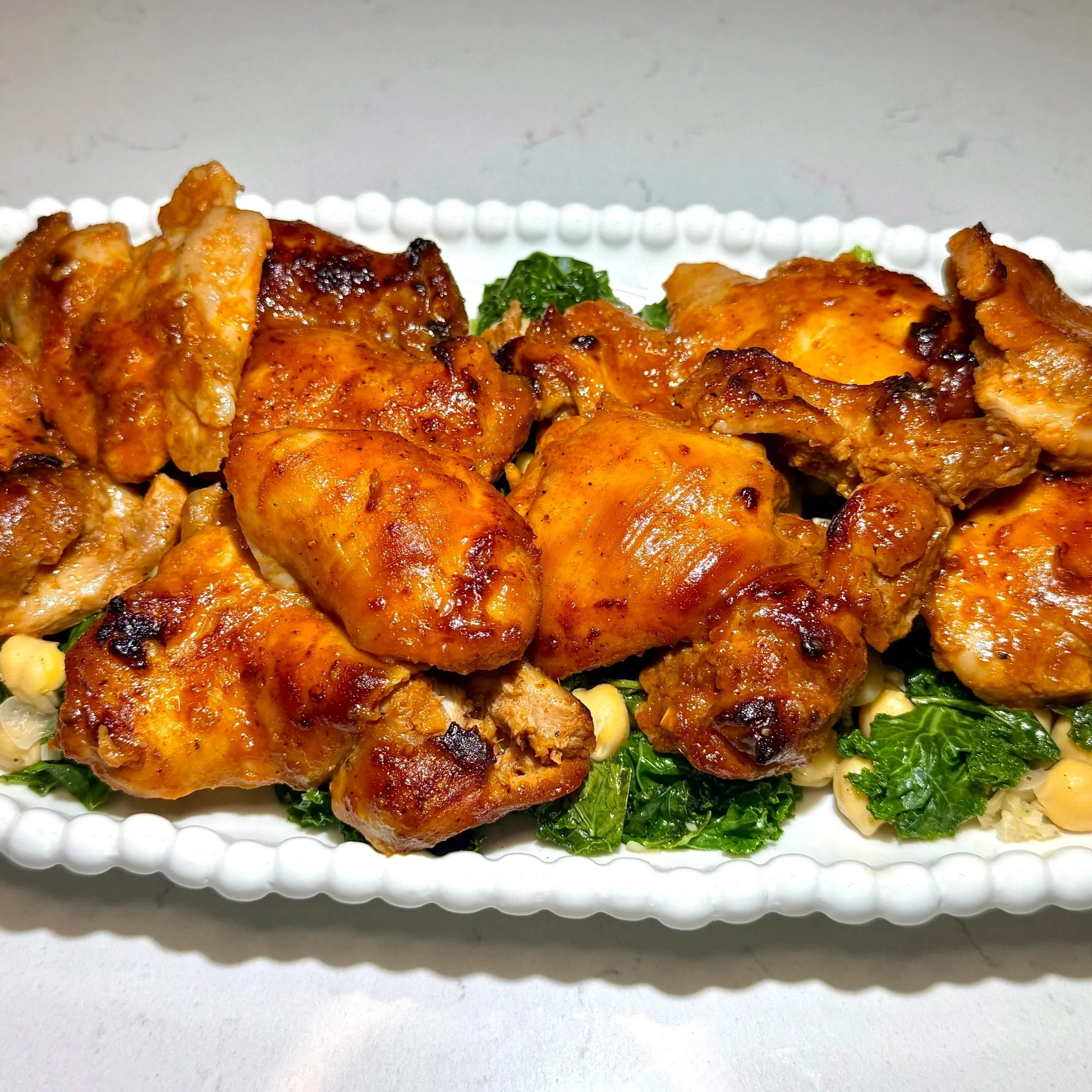 Close‑up of glossy gochujang chicken with kale and chickpeas.