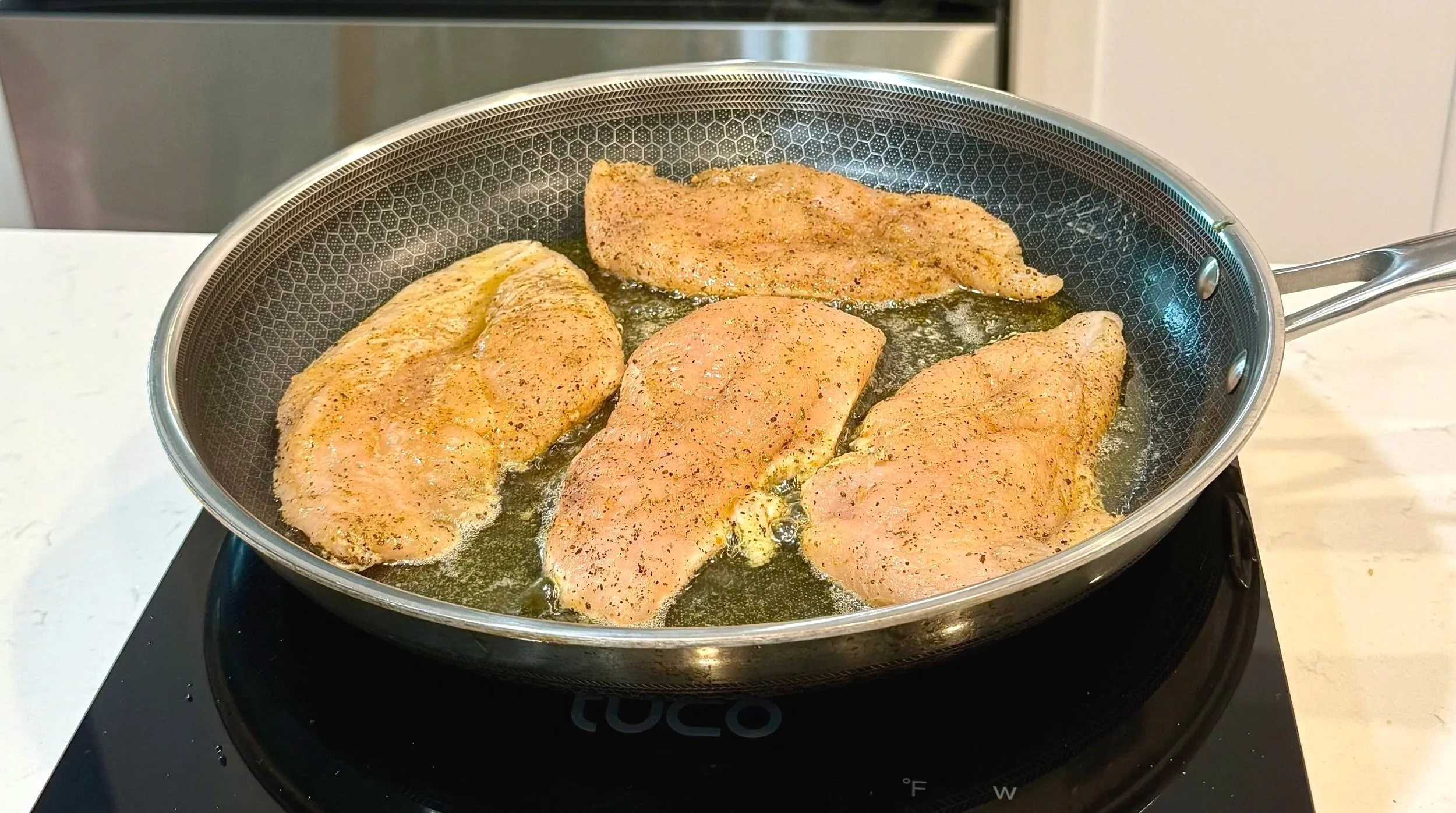 Chicken breasts searing in a skillet until golden brown on the first side.
