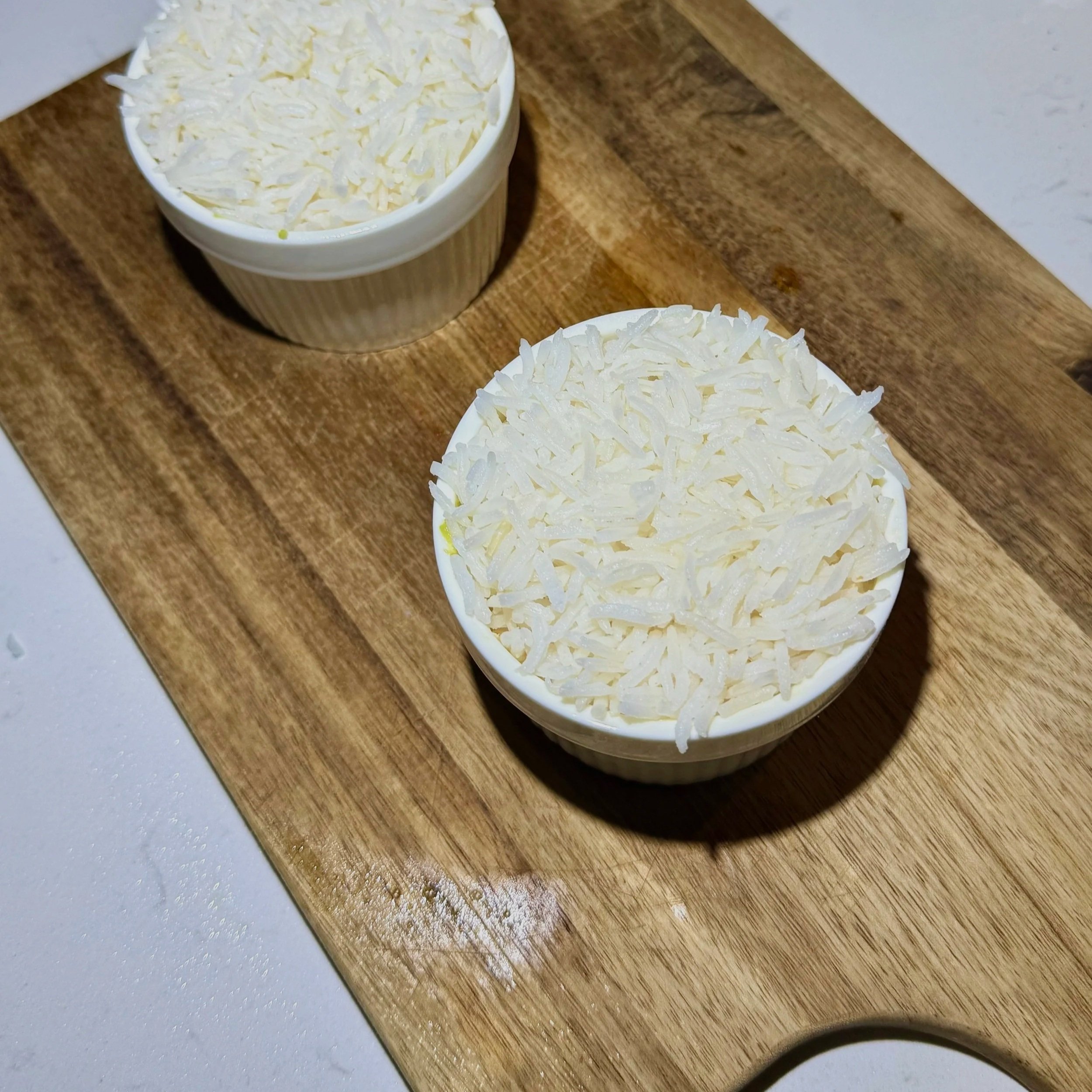 Cooked rice mixed with rice vinegar portioned into ramekins for assembling tuna rice stacks