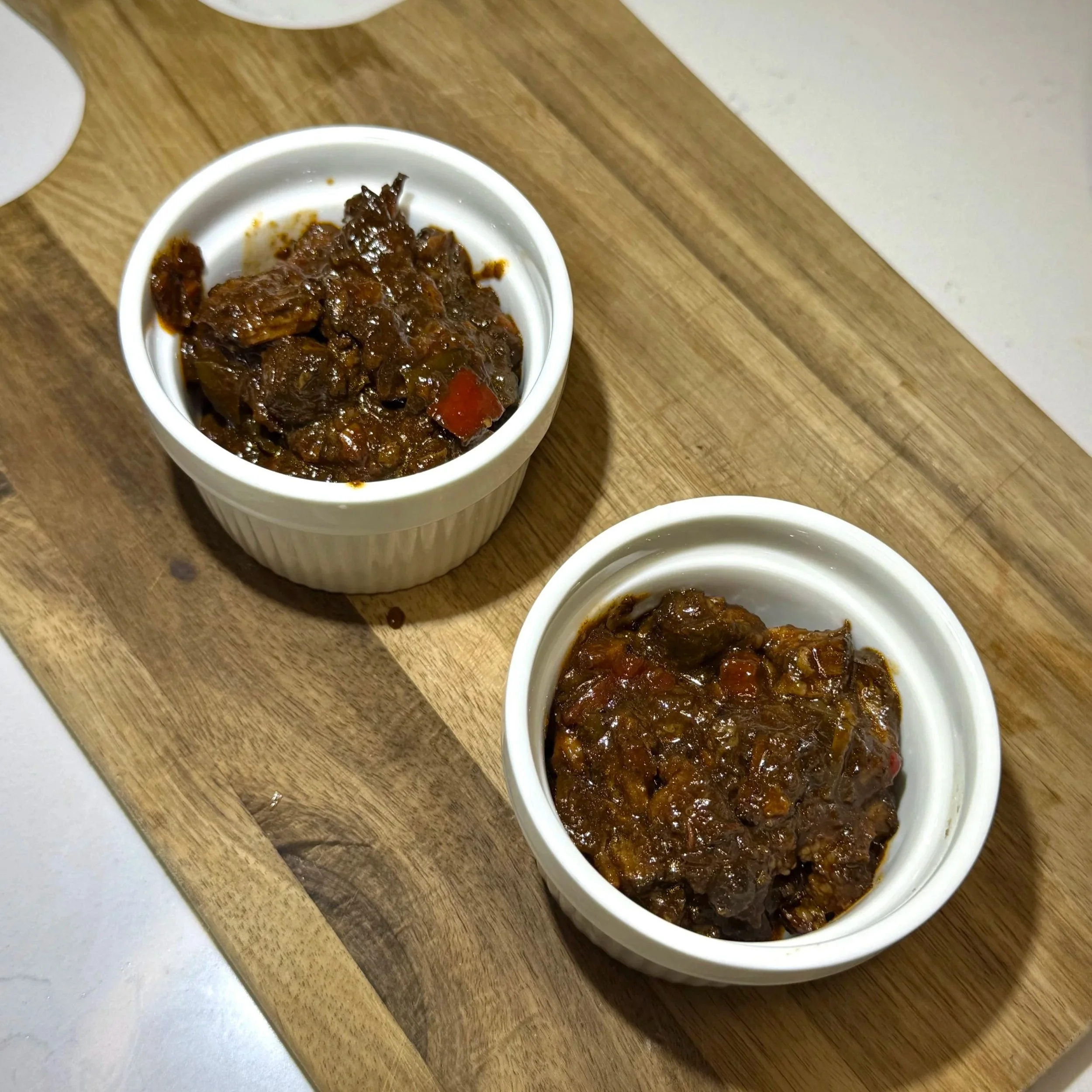 Oxtail placed in ramekins as the base layer for oxtail mac and cheese