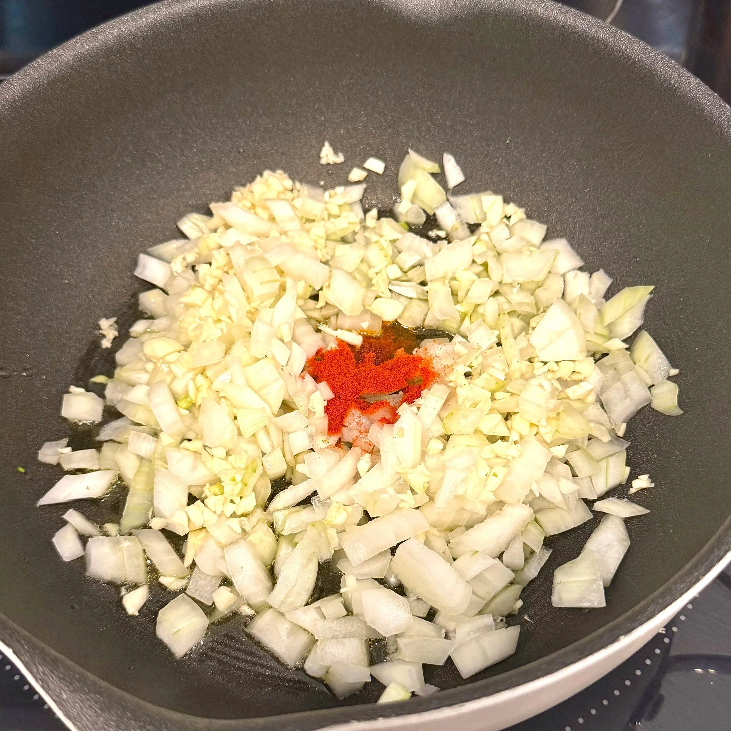 Diced onions sautéing in a pot with paprika sprinkled in the center.